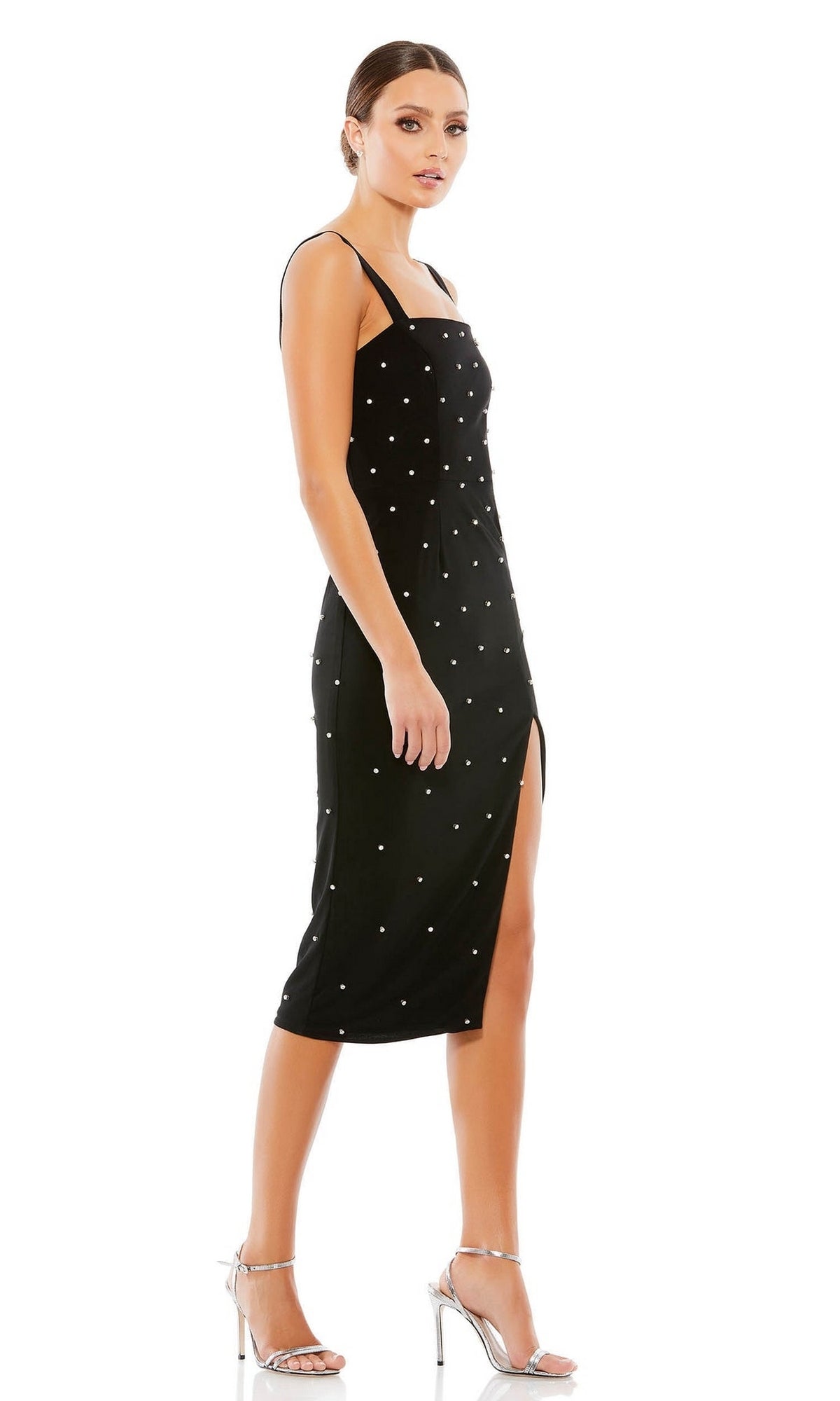A woman wearing the Short Wedding Guest Dress 70211 by Mac Duggal—a sleeveless black pearl dress with a square neck, white embellishments, and a side slit—paired with silver high-heeled sandals.